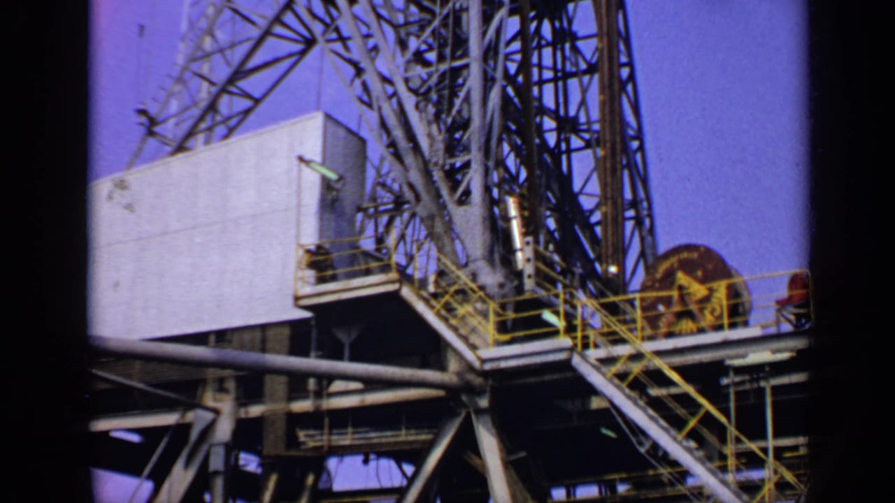 Low-angle view of refinery structure with pale equipment housing, yellow railings, and steel framework.