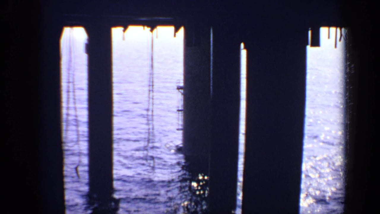 Dark pier supports frame calm sea with vertical hanging ropes.