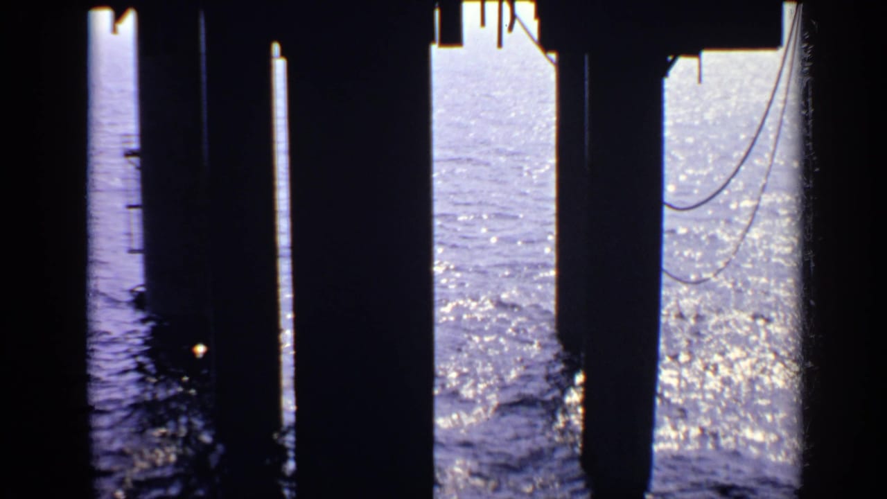 Dark pier pillars frame bright blue water with sunlight reflecting on small waves.