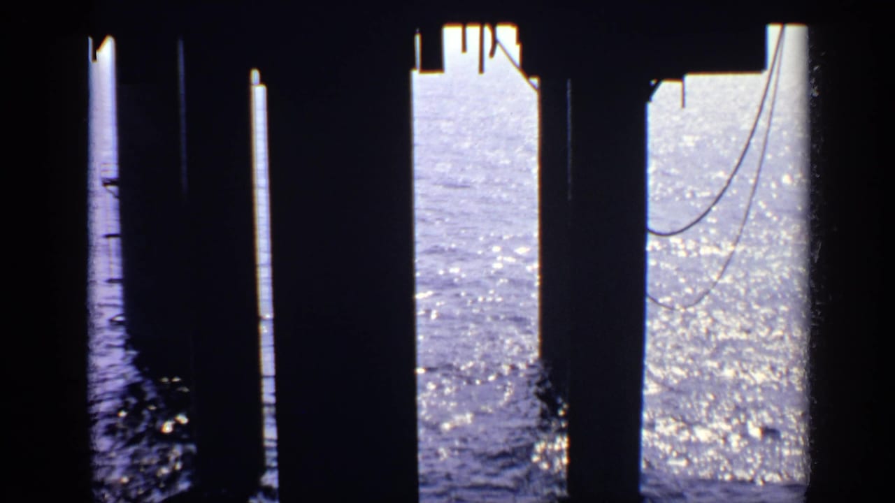 Pier supports and hanging cables stand in silhouette against sparkling water.