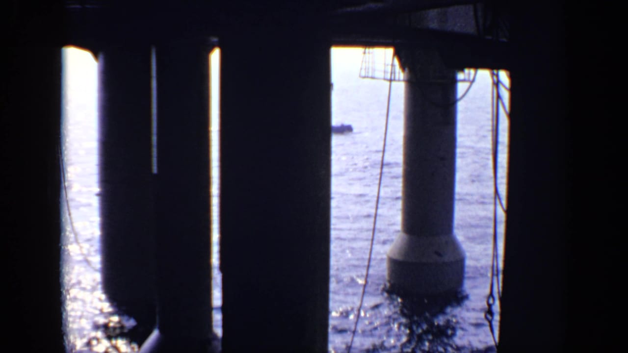 Dark structural supports frame sunlit water with a small distant vessel.