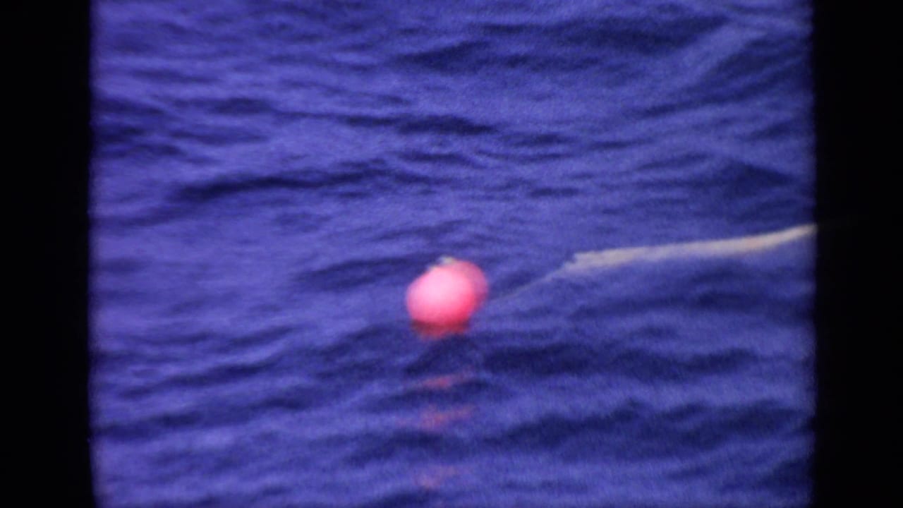 Red-pink round buoy floats on rippling blue water with a thin tether line.
