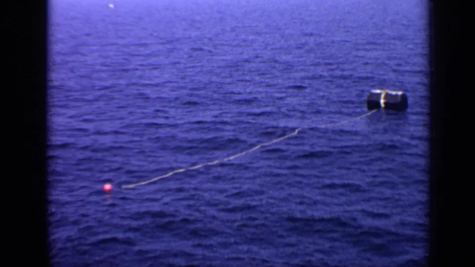 1970 United Kingdom 8mm frame showing a dark cylindrical float connected by a line to a small pink float on open water.