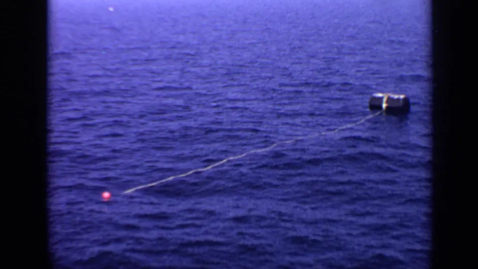 1970 United Kingdom 8mm frame showing a cylindrical buoy in open water, linked by a line to a small red marker buoy.