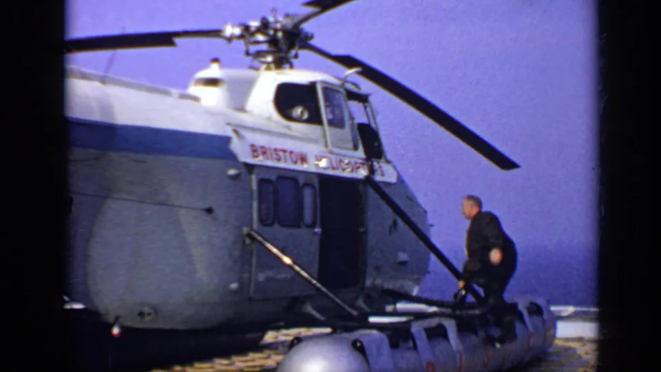 A 1970 United Kingdom frame shows a man boarding a Bristol Helicopters aircraft, with another figure partly visible inside.