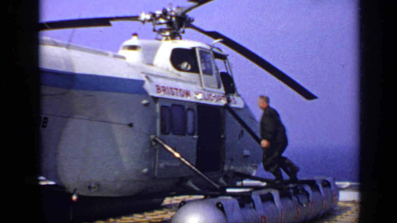 1970s United Kingdom 8mm frame showing a man climbing steps into a Bristow helicopter as the main rotor spins.