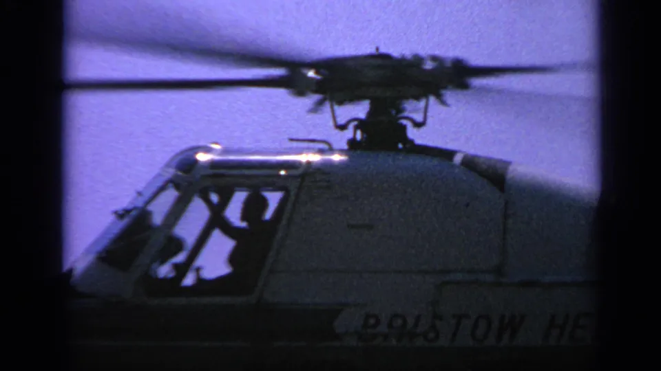 Close 8mm view of a Bristow helicopter cockpit in the United Kingdom, with a pilot silhouette and blurred rotor motion.