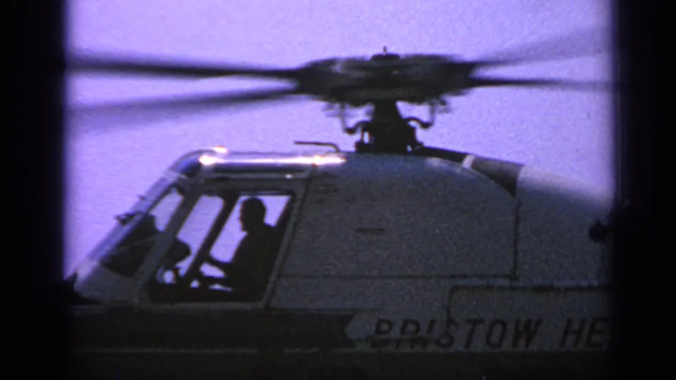 Close side frame of the Bristow helicopter with a visible cockpit figure, blurred rotor blades, and partial company lettering.