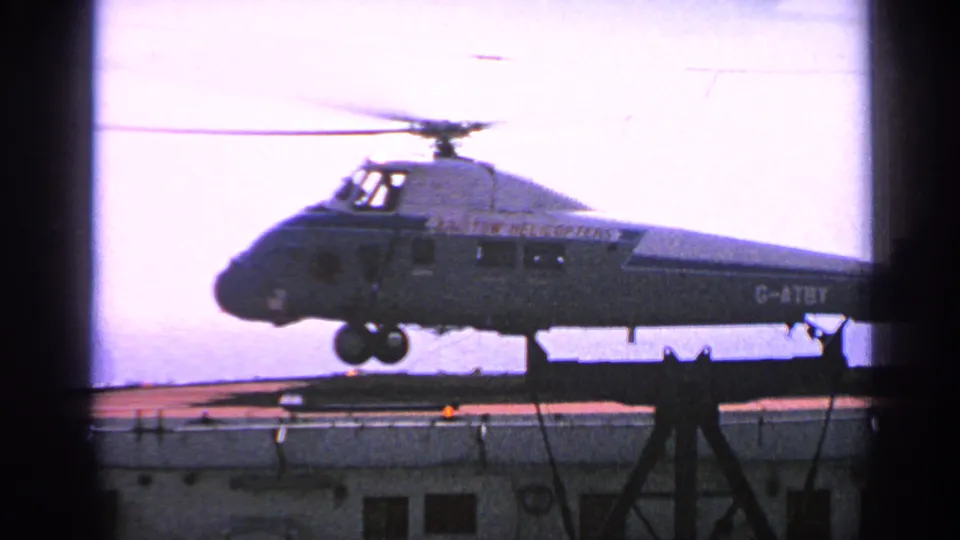 1970 United Kingdom 8mm frame showing the Bristol helicopter beginning lift-off from the helipad, with rotor blur and landing gear visible.