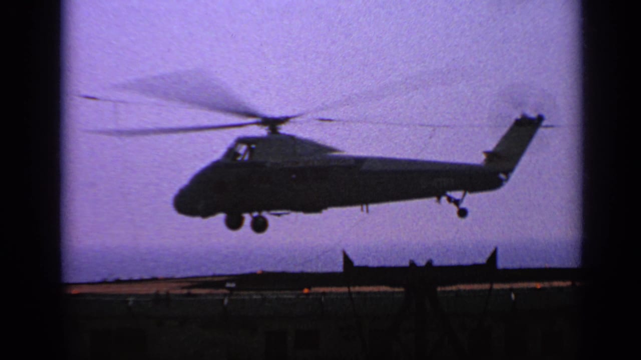 Silhouetted helicopter hovering above an aircraft carrier deck under a purple sky.