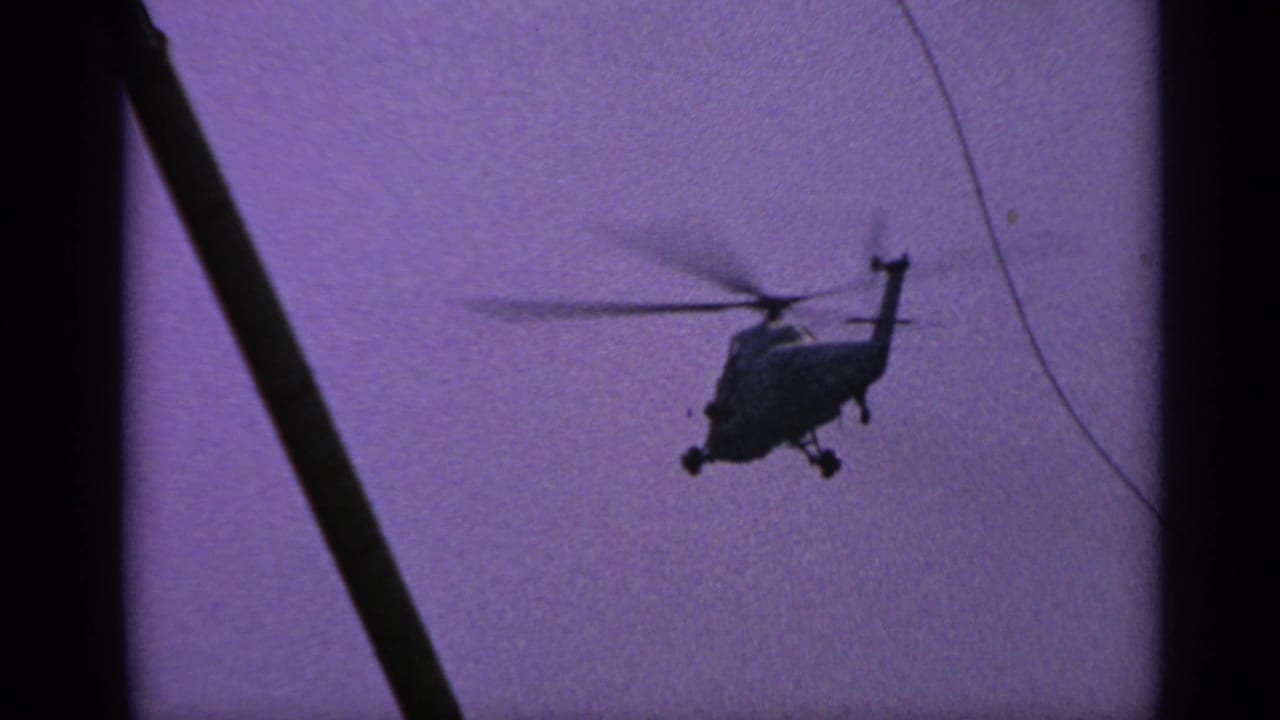 Helicopter in silhouette with spinning rotors, seen near a thin line in the sky.