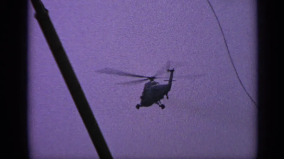 1970 United Kingdom 8mm frame of a helicopter silhouette with blurred rotors, purple sky, and sparse dark foreground lines.
