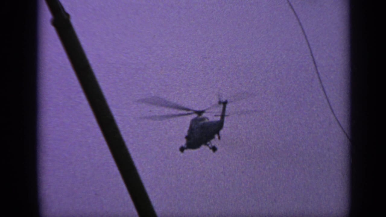 Small silhouetted helicopter in a purple sky behind a dark diagonal foreground pole.