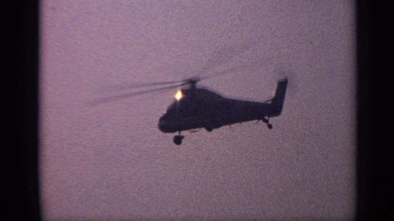 Helicopter silhouette flying against a hazy purple sky with rotor blur.