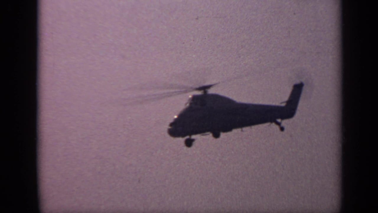 Dark helicopter profile in flight against an overcast, purple-tinted sky.