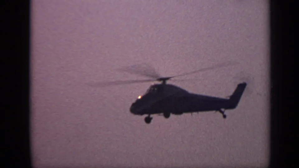 End-frame view from the 1970 United Kingdom 8mm clip, with the helicopter still silhouetted against a purple-tinted hazy sky.