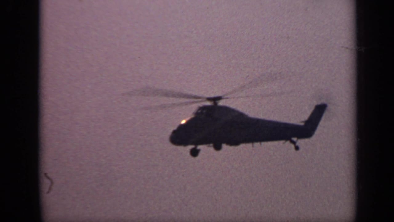 Large helicopter silhouette flying across a hazy sky over water.