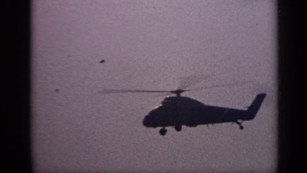 Helicopter seen in profile against a muted sky with water below.