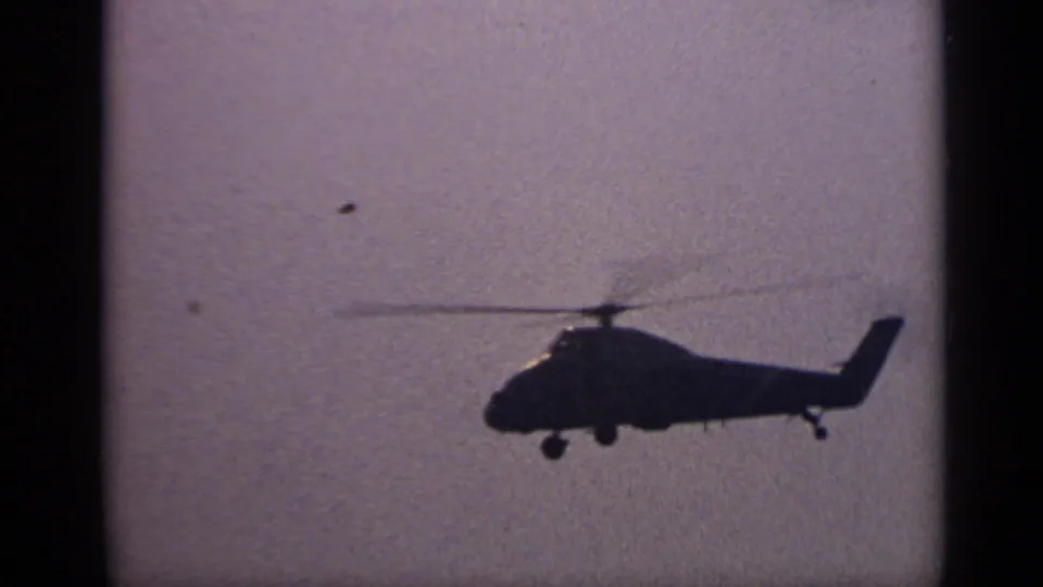 Profile view of a large helicopter moving across a hazy sky over water in United Kingdom archival 8mm footage.