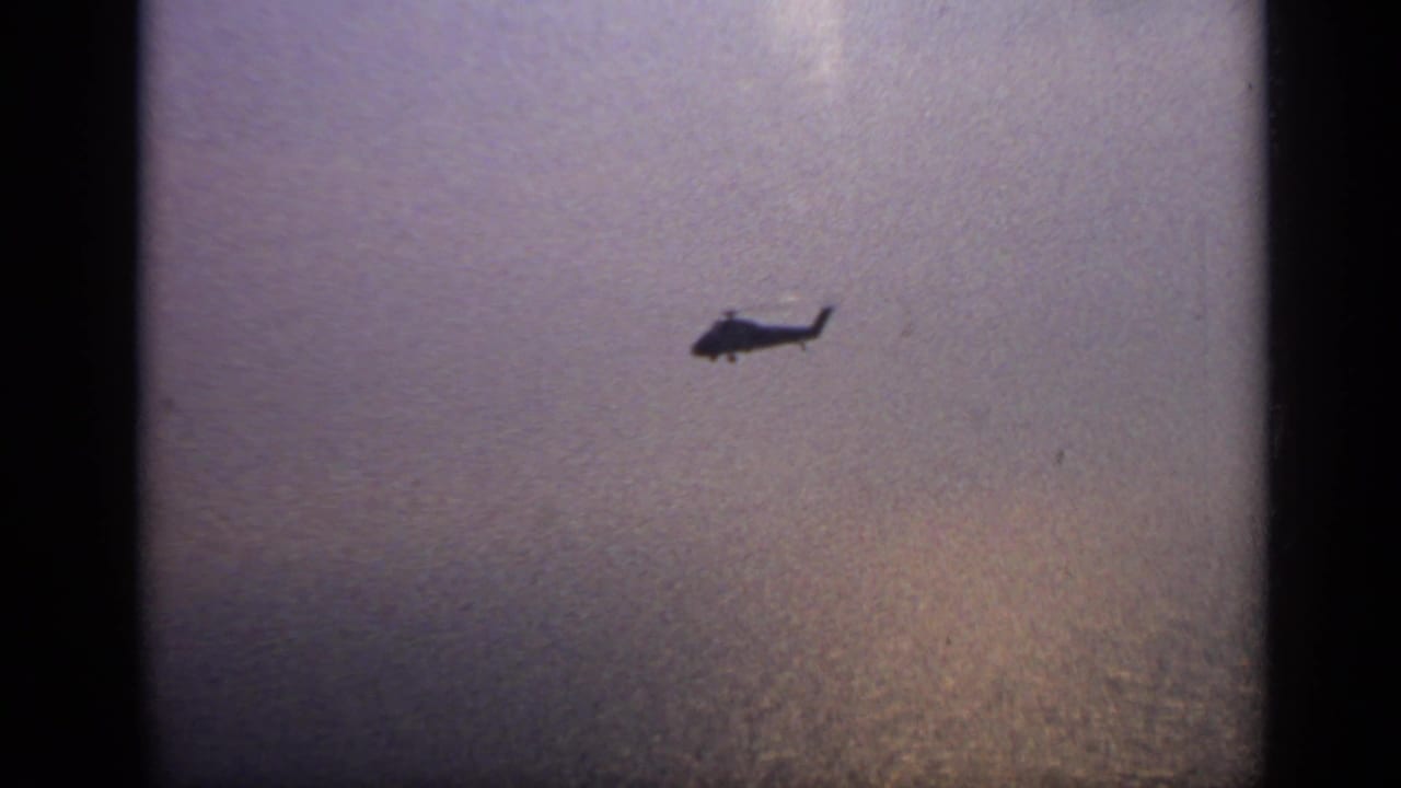 Small helicopter silhouette flying over hazy water and sky.