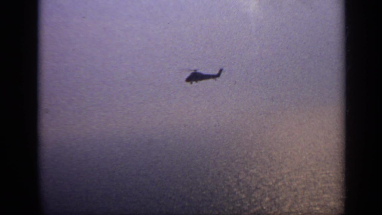 Distant helicopter silhouetted over hazy open water.