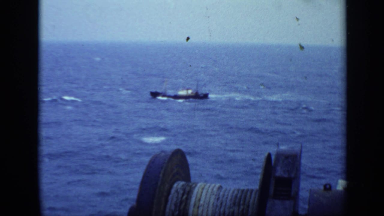 Small vessel on open sea with a cable spool in the foreground.