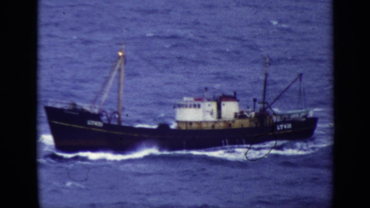 Dark fishing trawler crossing choppy water with white wake.