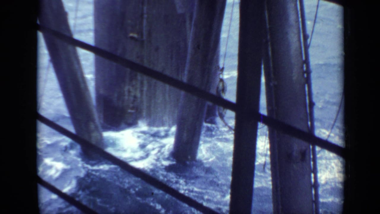 Waves churn around timber pier supports seen through diagonal metal railings.