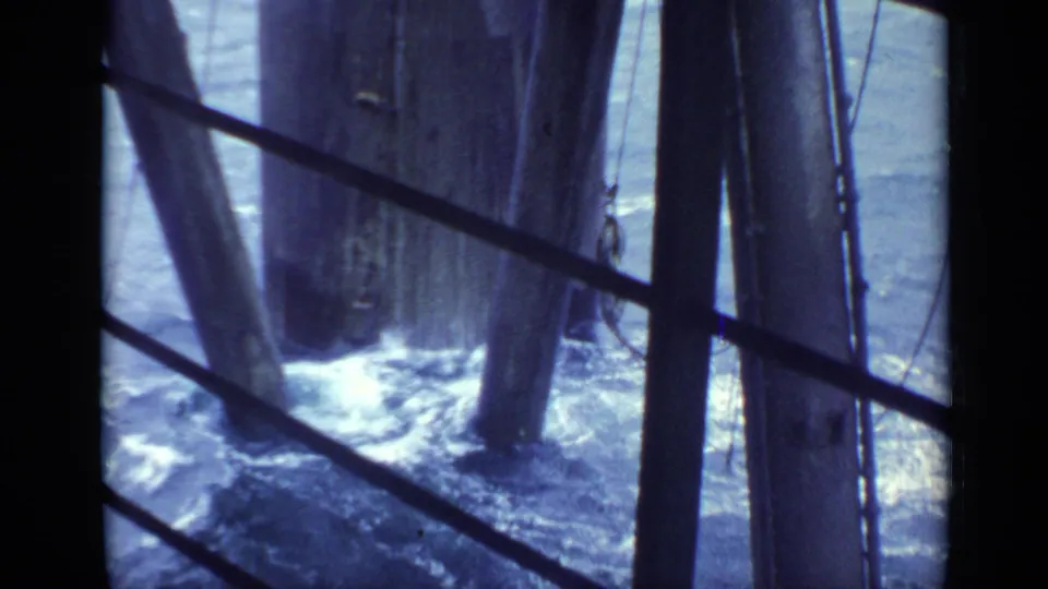 1970 United Kingdom 8mm view beneath a pier, with foaming waves around weathered timber supports behind diagonal railings.