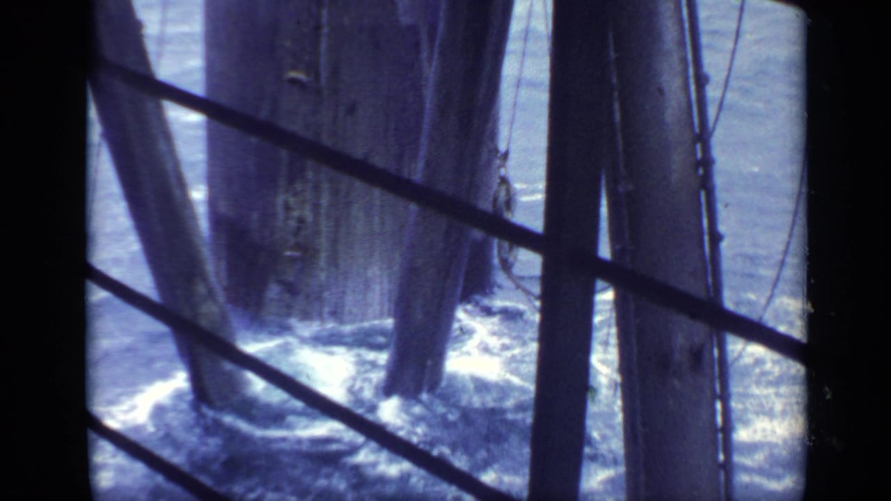 Handheld 8mm frame of waves splashing against wooden pier columns in the United Kingdom, seen through slanted metal rails.