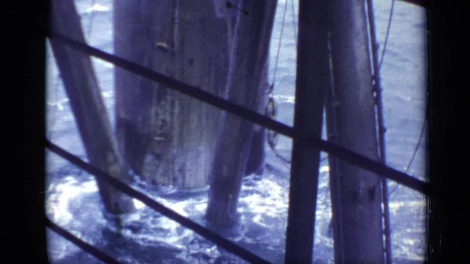 1970 8mm under-pier view with surf and white foam moving around vertical wooden support columns in a British coastal setting.