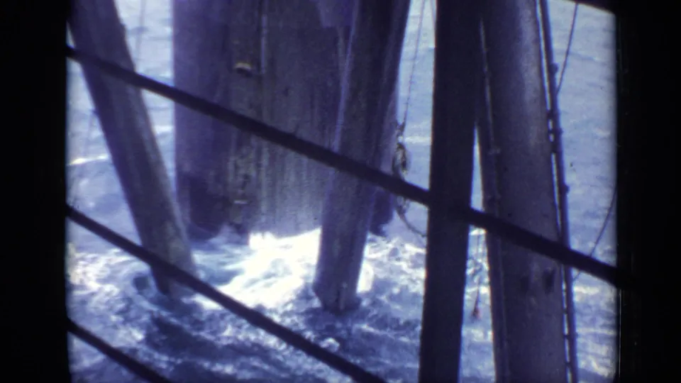 Vintage 8mm United Kingdom seaside frame showing water surging under a pier through dark railings and weathered timber supports.