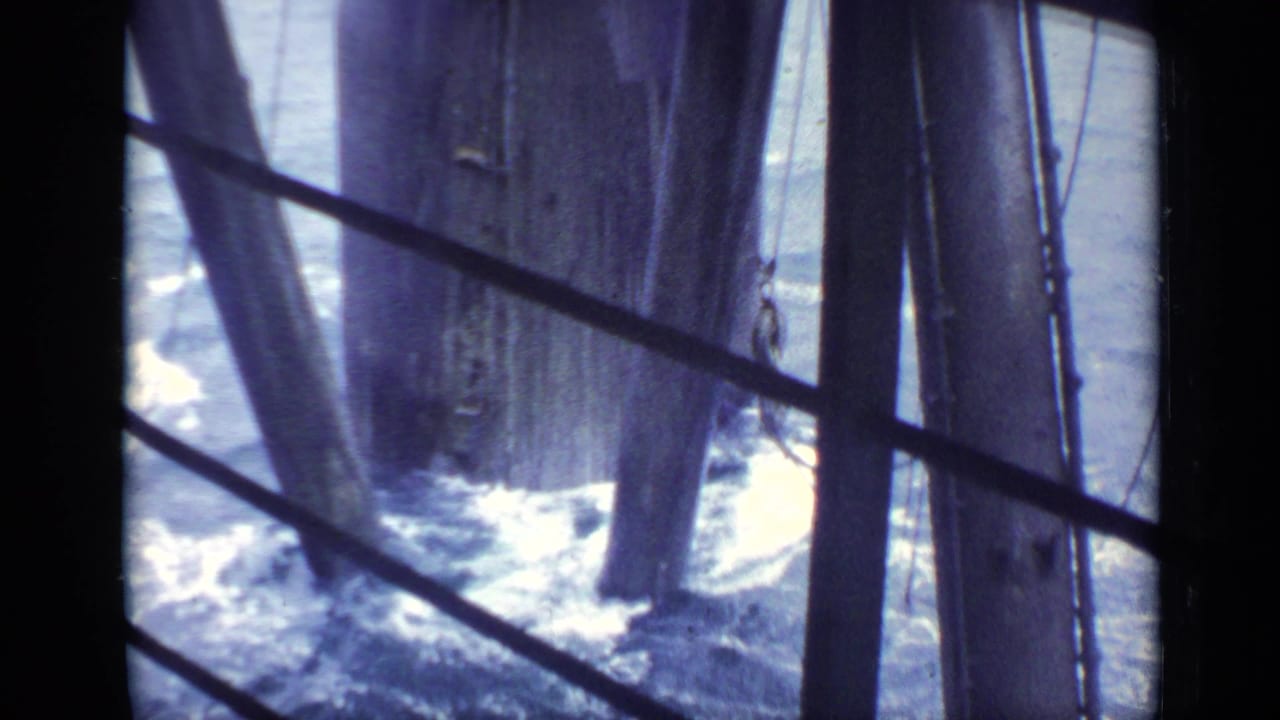 Choppy water below dark structural beams beside a large vessel or platform.