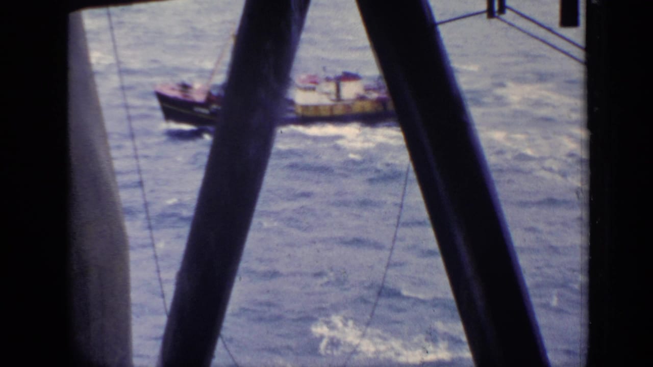 Small brown tugboat on choppy water seen through dark structural beams.