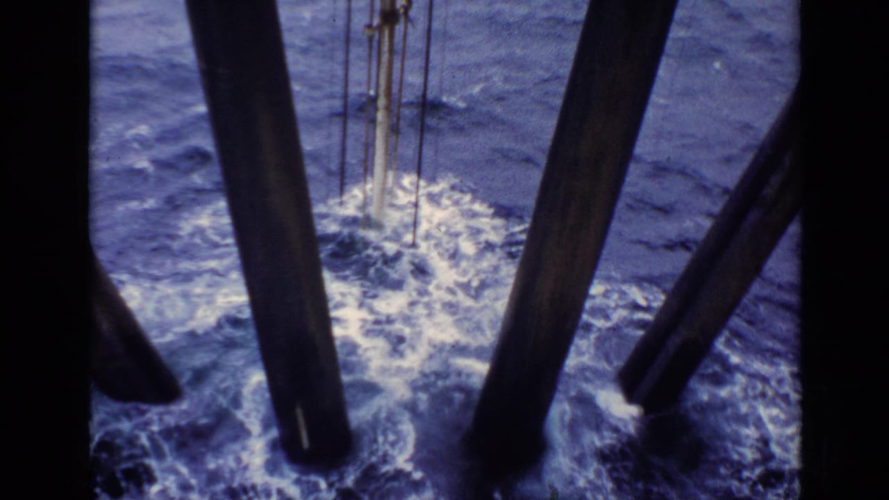 1970 United Kingdom 8mm frame looking down at foaming water around dark offshore or vessel supports.