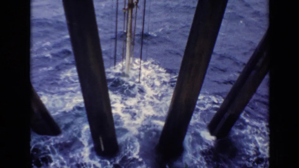 1970 United Kingdom 8mm frame looking down at foaming water around dark offshore or vessel supports.