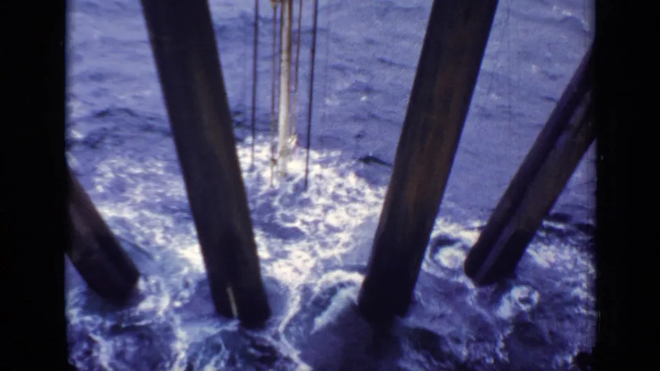 1970 United Kingdom 8mm frame showing choppy sea, white foam, and dark offshore or vessel supports below the camera.