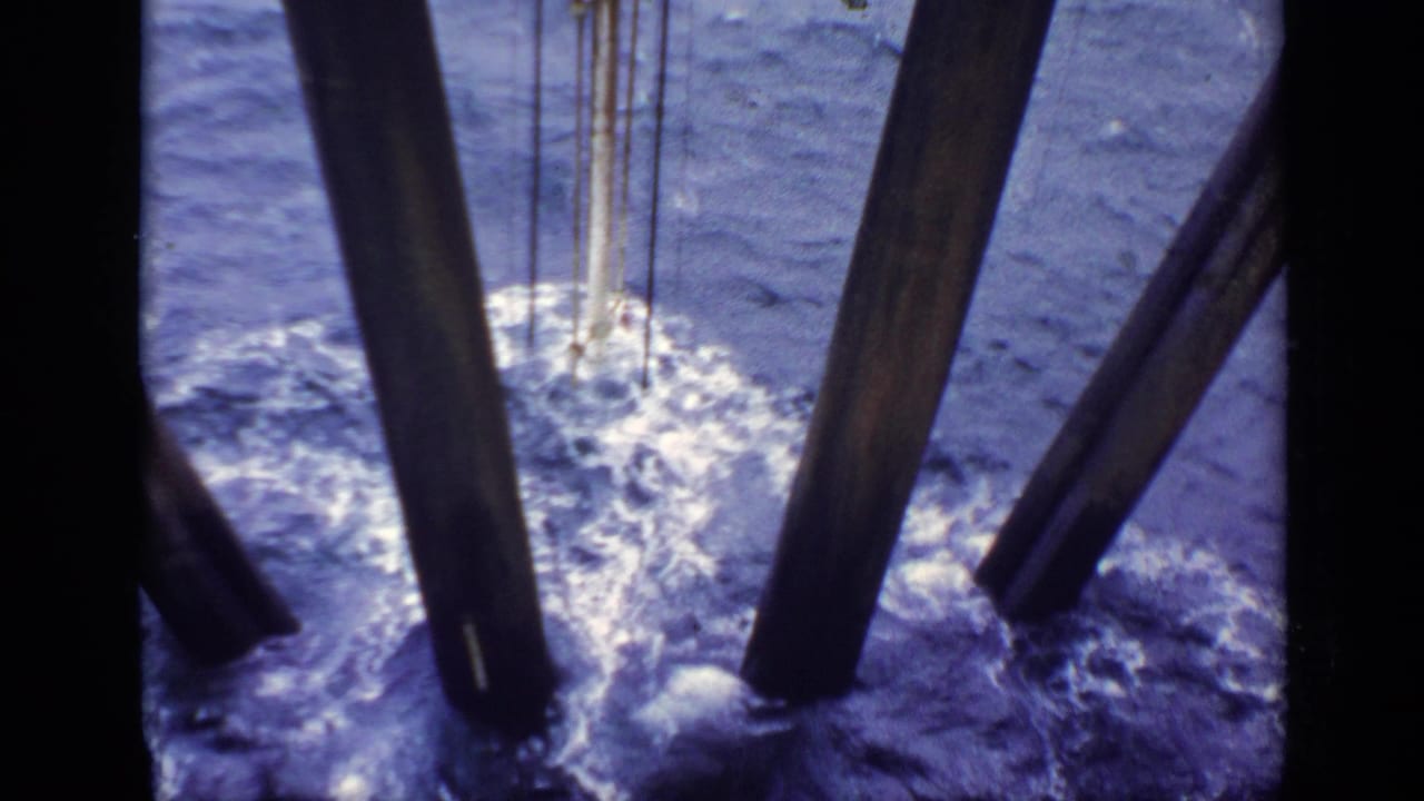 Choppy seawater splashes around heavy wooden piles beneath a structure.