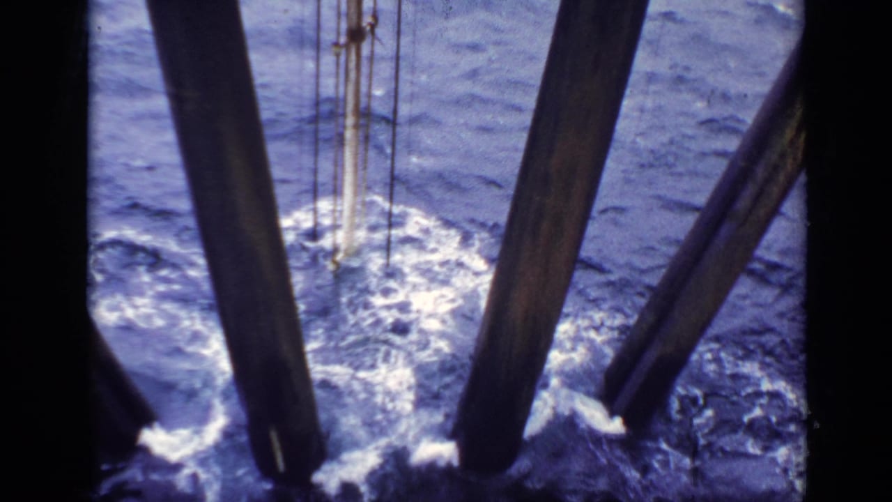 1970s United Kingdom 8mm frame of choppy sea water, foam, and structural piles viewed from close range.