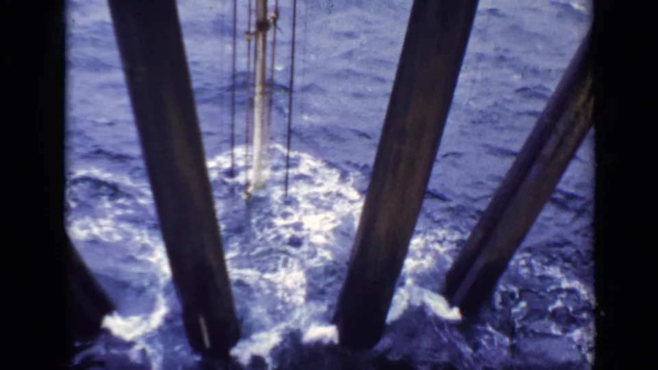 1970s United Kingdom 8mm frame of choppy sea water, foam, and structural piles viewed from close range.