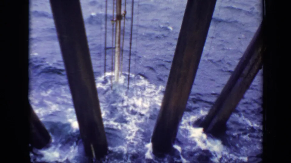 1970s United Kingdom 8mm close view of foaming choppy water between large wooden piles under a structure.