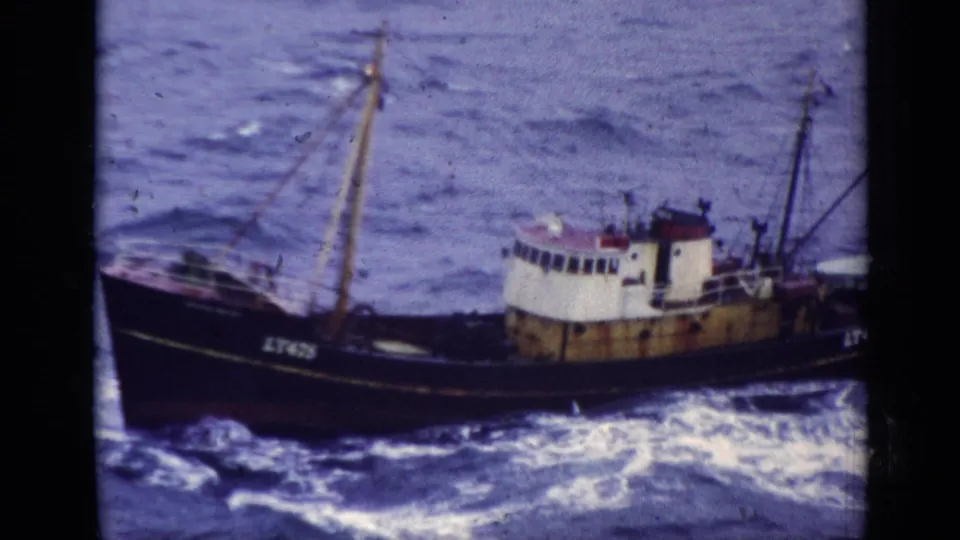 1970s United Kingdom 8mm frame showing a small fishing boat with a white cabin and dark hull on rough sea water.