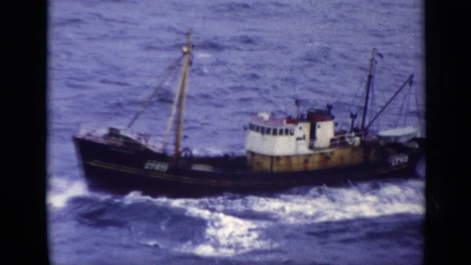 1970 United Kingdom 8mm frame of a weathered fishing trawler marked LT475 crossing choppy blue water.
