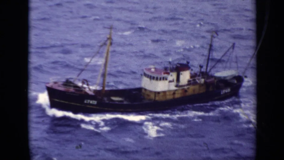 The trawler LT475 passes through blue open water, its dark hull and pale cabin softened by 8mm film texture.