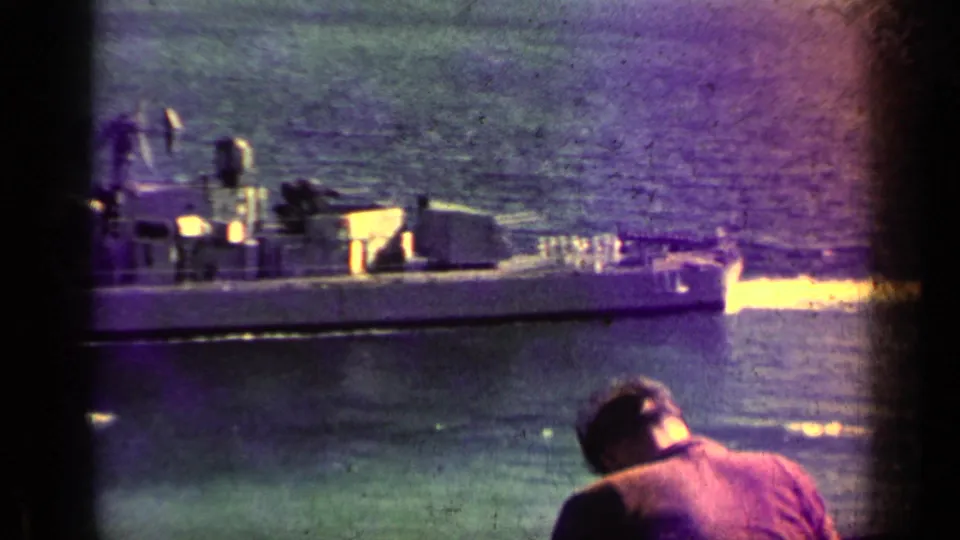 A 1962 Cuba 8mm frame shows part of a naval ship on the water while a foreground man leans toward the view.