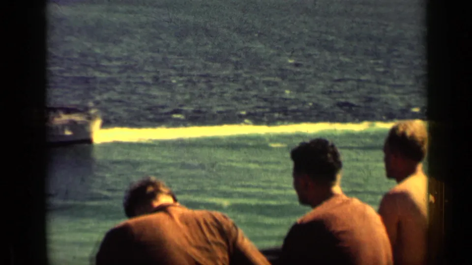 1962 Cuba 8mm frame showing men on a ship deck facing the sea, with a wake and distant water beyond.