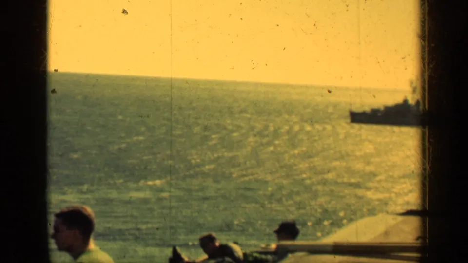 1962 Cuba 8mm frame from a ship deck, with men partly visible and a distant naval-looking vessel across sunlit water.