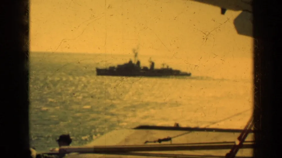 1962 Cuba 8mm frame showing a distant naval-looking ship on hazy water, filmed past the deck rail of another vessel.