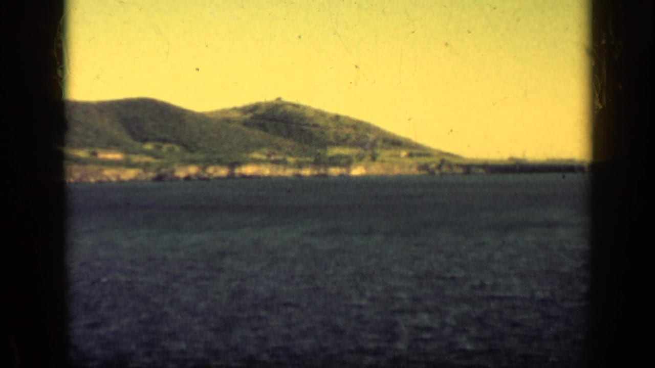 Coastal mountains across blue water, viewed through dark vertical window edges.