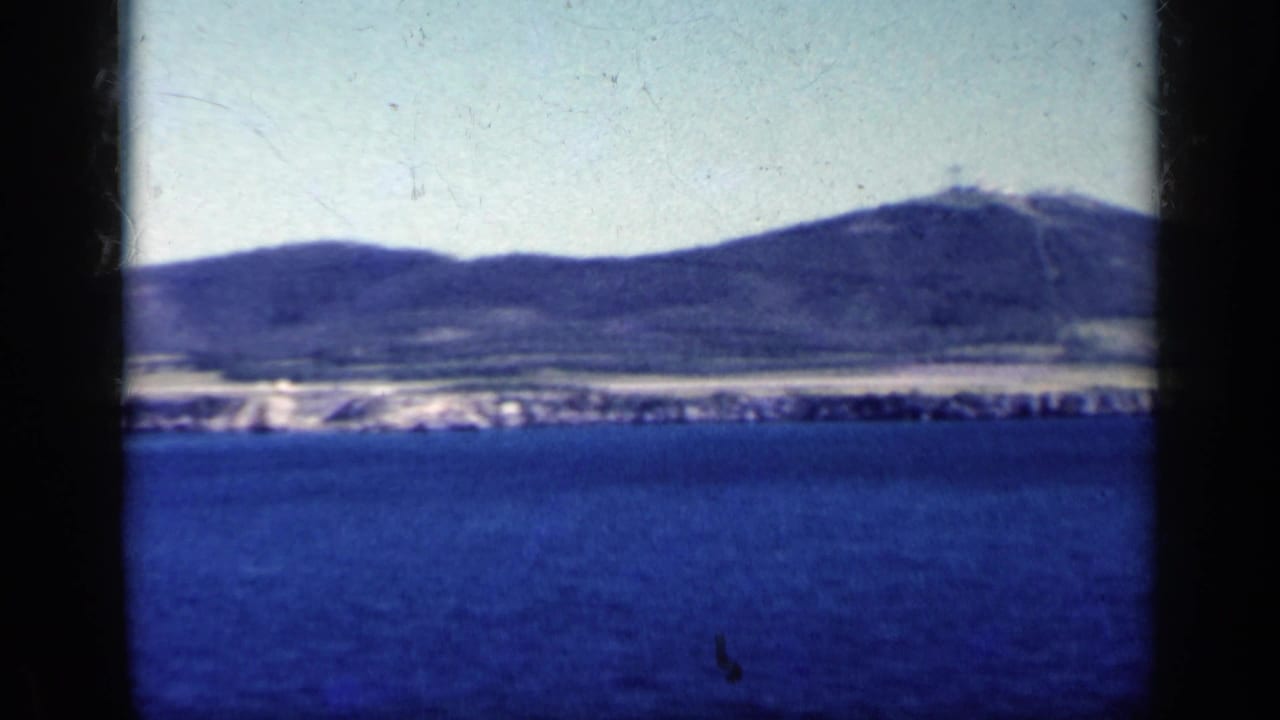 Deep blue water before a distant hilly shoreline, bordered by dark 8mm frame edges.
